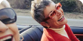 Woman in red sweater and sunglasses laughing in a car